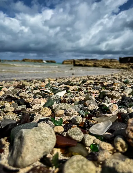 Sea glass and stones along the shoreline at Glass Beach in Bermuda under cloudy skies.