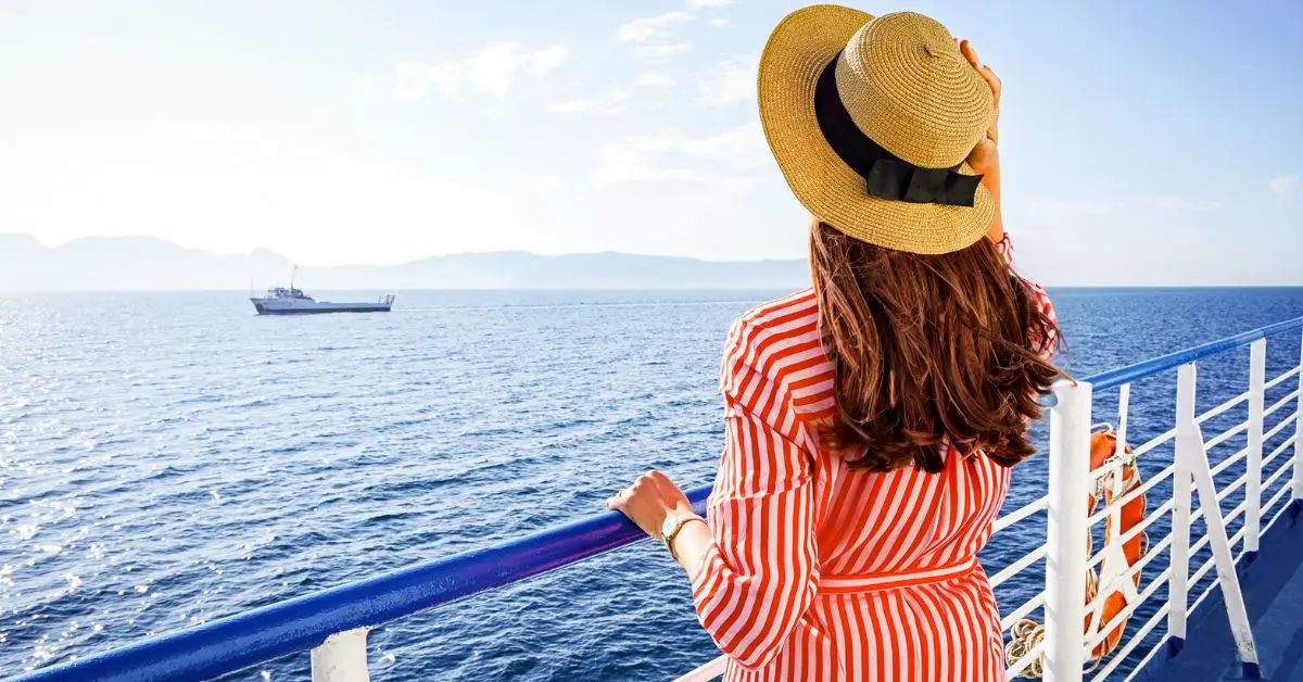 featured blog image | cruise outfits for women | women standing on a cruise deck staring out in the ocean in a striped red dress and a sun hat