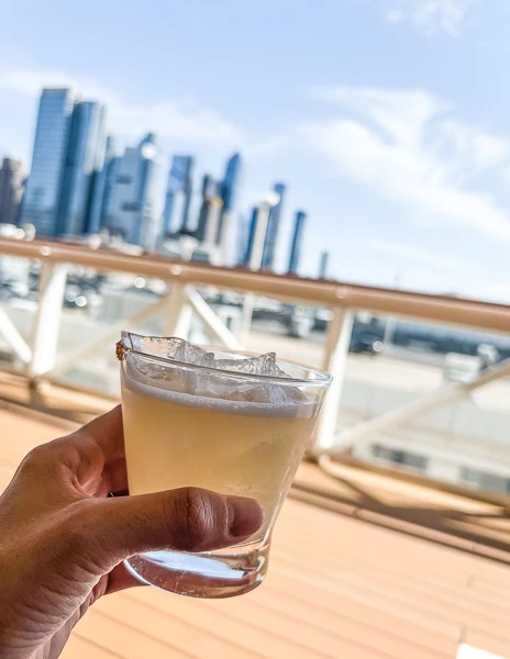 hand holding a cocktail with nyc skyline in the background