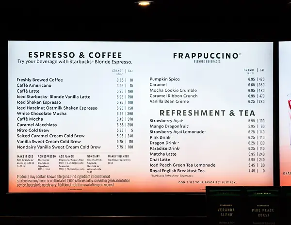 Photo of the Starbucks menu aboard Norwegian Cruise Line as of May 2025, showing prices for espresso drinks, Frappuccinos, and teas. Menu includes items like brewed coffee, lattes, iced drinks, cold brews, and refreshers, with prices ranging from $3.85 to $7.25.