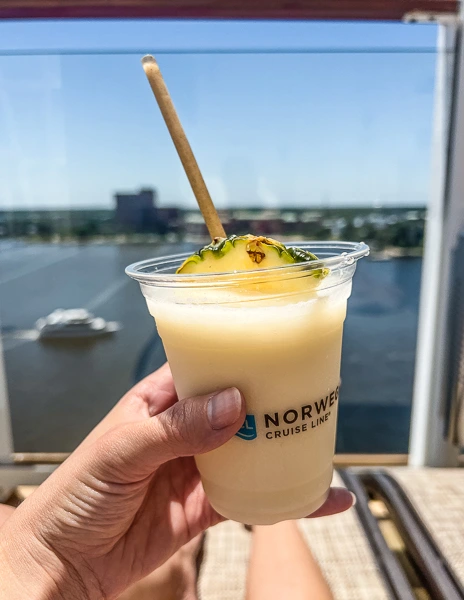 holding a pina colada with the norwegian cruise line logo on cup