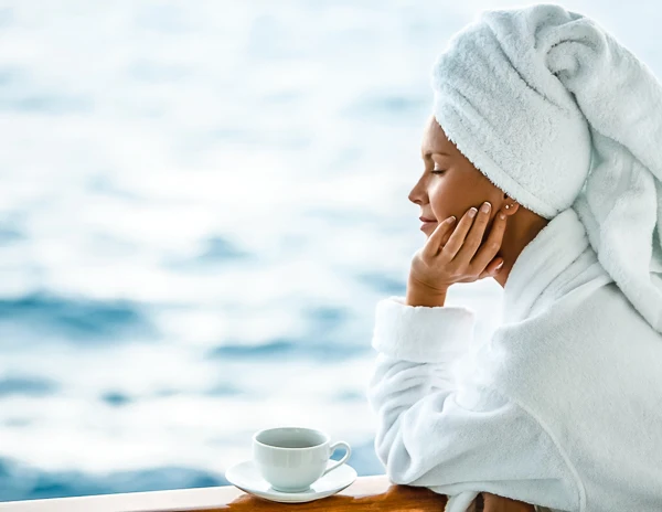 wearing wearing a robe and towel on her head enjoying coffee in her cruise ship balcony