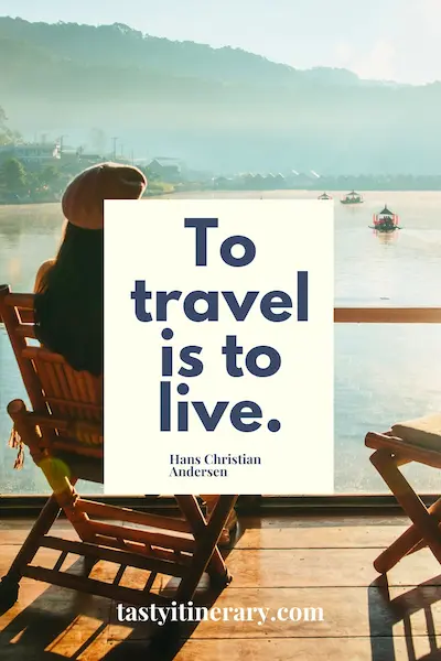 graphic: A woman sits on a wooden chair overlooking a calm river at sunrise, with misty hills and small boats in the background. The quote “To travel is to live.” by Hans Christian Andersen
