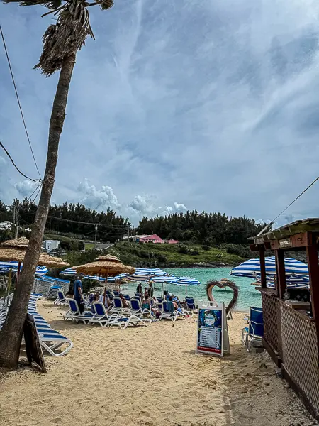 Entrance to Tobacco Bay Beach in Bermuda with lounge chairs, umbrellas, a beach bar, and turquoise water.