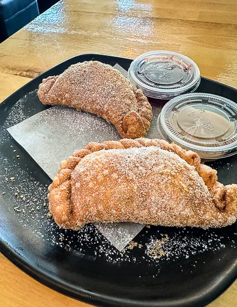 Two cinnamon sugar–coated dessert empanadas, including cheesecake and apple pie flavors, served with dipping sauces at Lord Empanada in Monrovia.