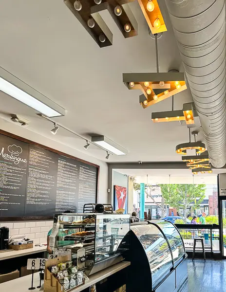 View of Merengue Bakery’s front counter and pastry case, with marquee “EAT CAKE” lights and a view out to Old Town Monrovia.