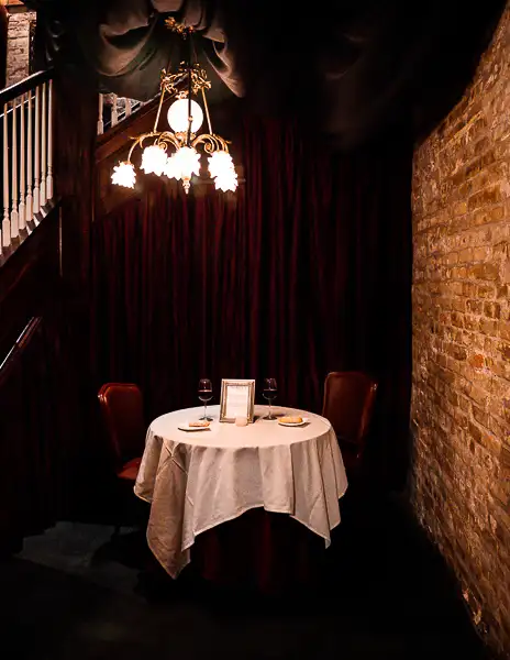 two person table set up with bread and wine in a dark corner