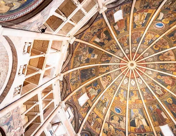 Visitors inside the Parma Baptistery viewing fresco-covered walls and domed ceiling with religious artwork