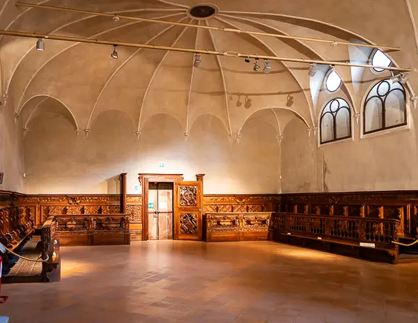 Room inside the former convent of St. Paul in Parma, featuring vaulted ceilings and wooden pew-style benches along the walls