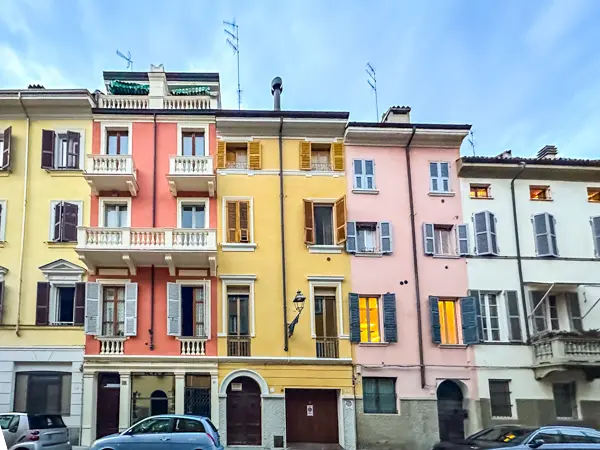 Row of colorful pastel buildings in Parma, Italy, with shuttered windows and balconies at dusk