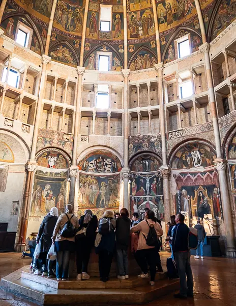 Visitors inside the Parma Baptistery viewing fresco-covered walls and domed ceiling with religious artwork