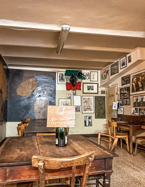 The interior of Osteria del Sole in Bologna, Italy, featuring rustic wooden tables, chairs, and walls adorned with vintage photos and memorabilia.