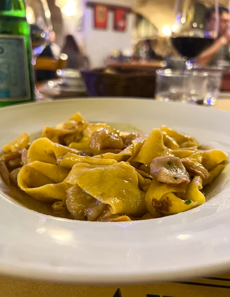 A plate of Pappardelle with porcini mushrooms and chestnuts, served at Cantina Bentivoglio in Bologna, showcasing fresh, golden pasta and a rich sauce.