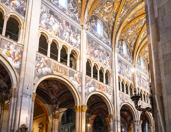 Interior arches and upper frescoes of Parma Cathedral decorated with detailed biblical scenes and gold-painted ceilings