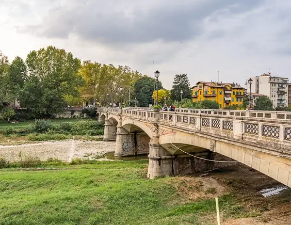 View of Ponte Verdi bridge in Parma, Italy, with people walking across and colorful buildings in the background