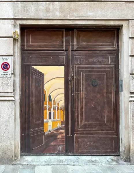 Wooden door in Parma painted with a trompe-l'œil mural showing an arched hallway, creating the illusion of an open interior space
