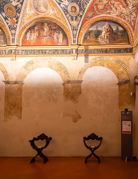 Frescoed walls and arches inside the Chamber of St. Paul in Parma, with two wooden chairs placed below the artwork