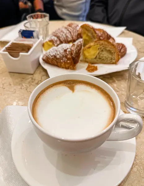 A cappuccino with frothy milk served alongside freshly baked cornettos at a café in Bologna, Italy