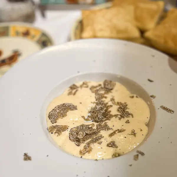 Poached egg with potatoes topped with Parmigiano Reggiano foam and shaved truffles, served with Prosciutto di Parma and torta fritta in the background at Gallo d’Oro in Parma