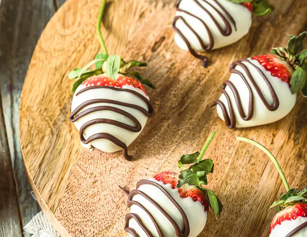 Close-up of chocolate-covered strawberries with white chocolate coating and dark chocolate drizzle, displayed on a round wooden board.