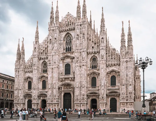 Front view of the Milan Cathedral (Duomo di Milano) with crowds gathered in the plaza below, showcasing its ornate Gothic architecture.