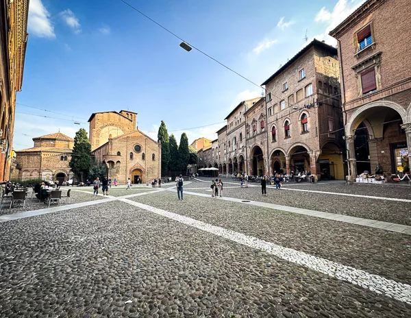 A wide view of Piazza Santo Stefano in Bologna, showcasing its cobblestone square, historic buildings, and visitors enjoying the open space.