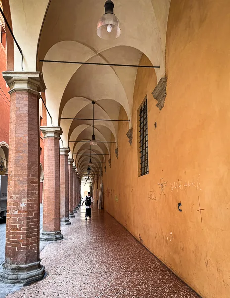 A view of Bologna’s porticoes with pale orange walls and intricate arched ceilings, extending into the distance.