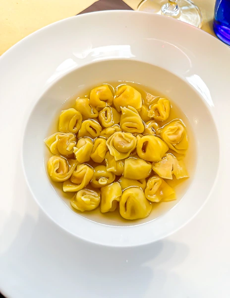 A bowl of tortellini en brodo, featuring small, handmade tortellini pasta served in a clear, golden broth, presented in a white dish. This classic dish from Bologna, Italy, highlights the region’s culinary tradition.