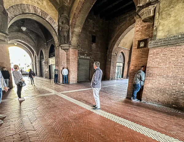 The Whispering Walls under the porticoes of Palazzo del Podestà in Bologna, Italy, with people standing in the corners to test the acoustic effect.