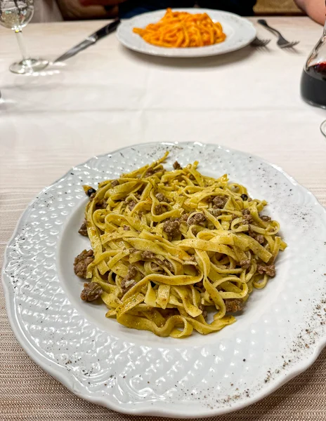 A plate of Pappardelle al Cinghiale (wild boar pasta) served at Trattoria Dardano in Cortona, Italy, showcasing fresh pasta topped with hearty, savory meat sauce.