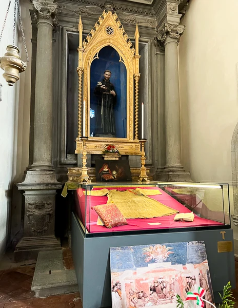 A display inside the Convento di San Francesco in Cortona, Italy, featuring St. Francis of Assisi’s tunic and other relics in a glass case beneath an ornate golden shrine.