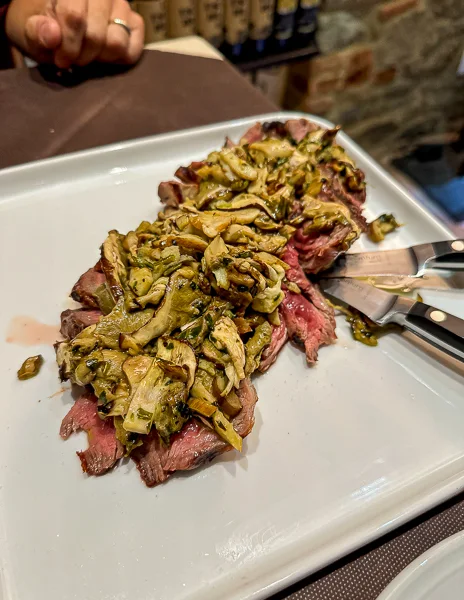 A perfectly cooked steak topped with porcini mushrooms, served at Osteria Le Rughe di Cortona, Italy, showcasing a rustic and hearty Tuscan dish.