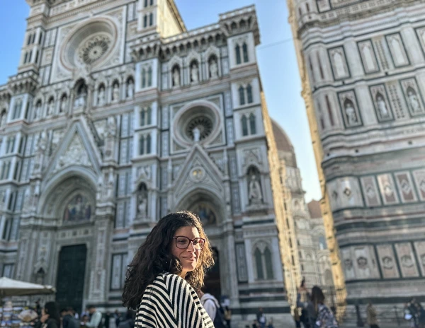 A woman (kathy) standing in front of Florence Cathedral during sunrise, with the intricate facade and bell tower glowing in the soft morning light.