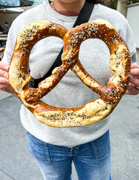 girl holding up a large bavarian prezel with everything seasoning at universal studios hollywood