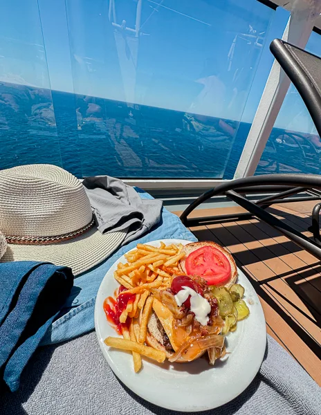 a plate of burger and fries siting on a chair facing the ocean on a cruise