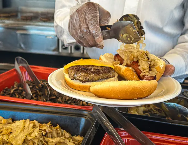 adding toppings to a burger and hot dog on a plate at the mast grill on celebrity solstice