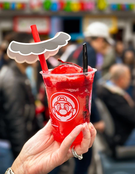 hand holding up strawberry and ice cream soda in a cup with cut out mustache on the straw | mario strawberry soda from universal studios hollywood