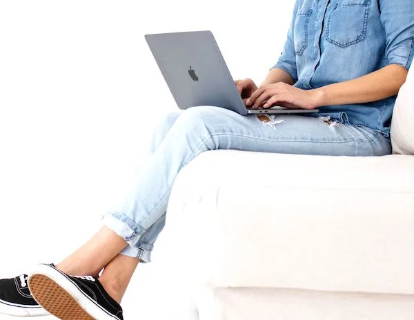 woman sitting on sofa with her legs crossed typing on a laptop sitting on her lap