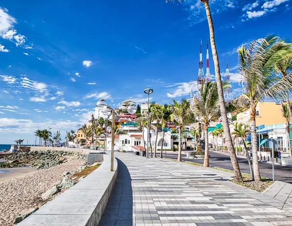 El Malecón boardwalk in Mazatlán, lined with palm trees, colorful buildings, and a beach on a sunny day. El Malecón boardwalk in Mazatlán, lined with palm trees, colorful buildings, and a beach on a sunny day.