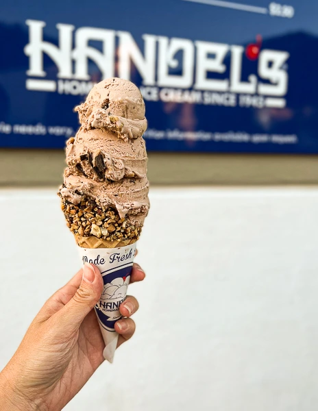 a hand holding an ice cream cone with nuts with a large scoop of handel's french silk pie ice cream