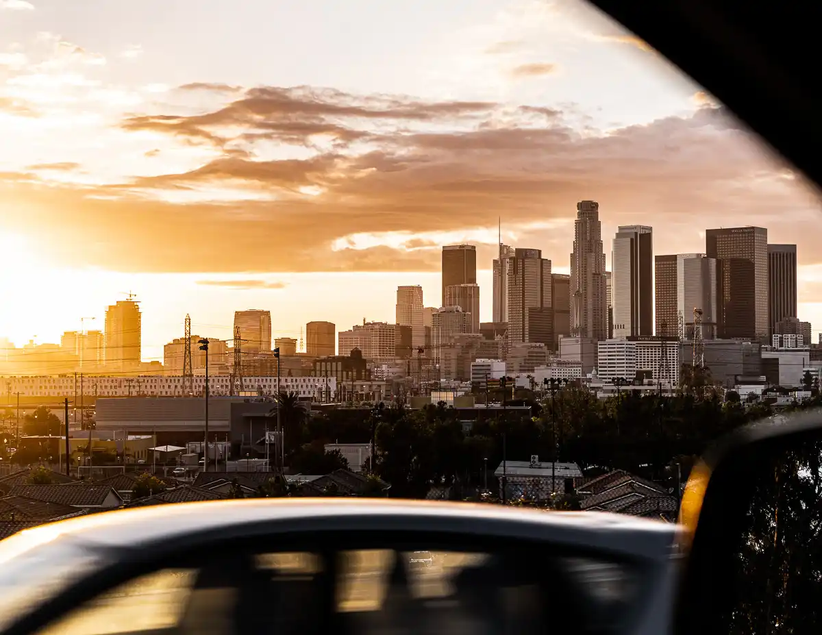 car driving past a skyline view of downtown los angeles at sunset