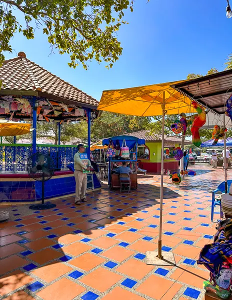 An outdoor area of the Mazatlán cruise terminal with colorful tile flooring, yellow umbrellas, and vendors selling local goods