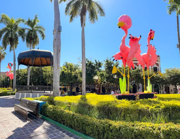 Plaza Machado in Mazatlán with vibrant pink flamingo statues and palm trees surrounding a central gazebo