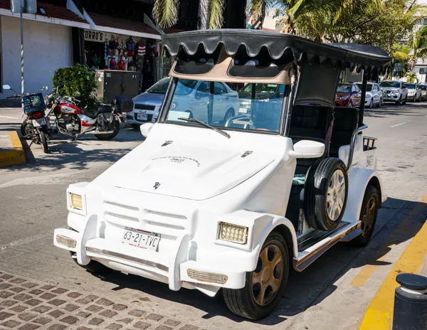 A white Pulmonia taxi with a black canopy parked on a street in Mazatlán's downtown area.