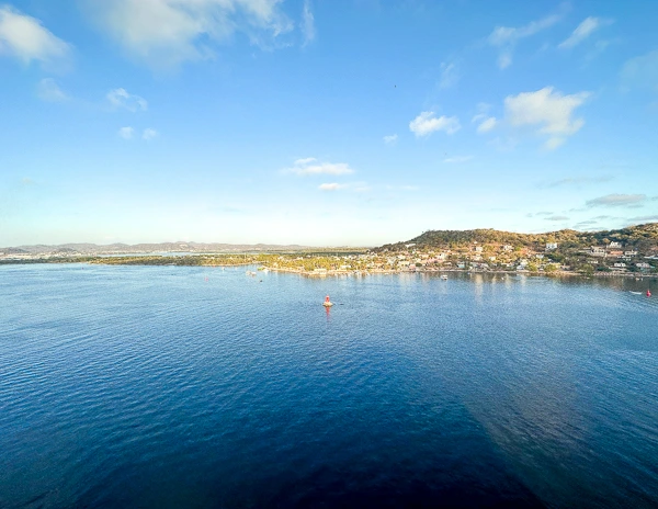 A view from the side of a cruise ship docked at Mazatlán port, overlooking the calm waters and distant shoreline.