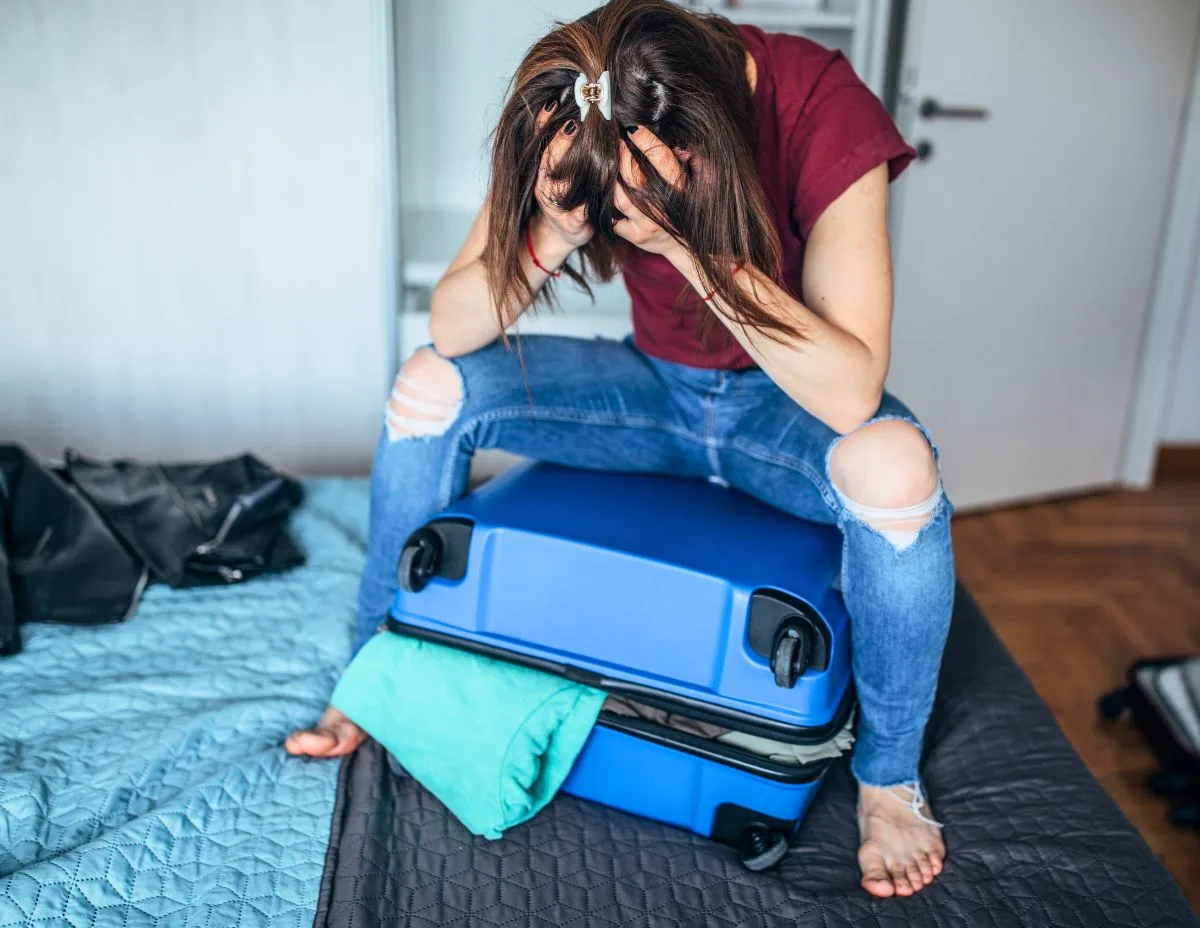 a frustrated female sitting on a large overpacked suitecase