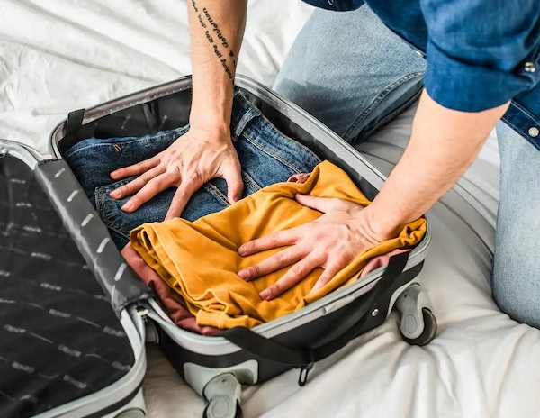 man stuffing clothes into suitcase