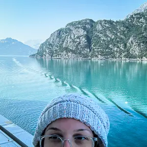 picture of half of kathy's head with knitted hat on with glacier bay in alaska in the background