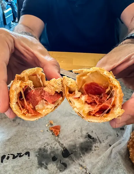 an empanada broken in half with the pepperoni and cheese filling