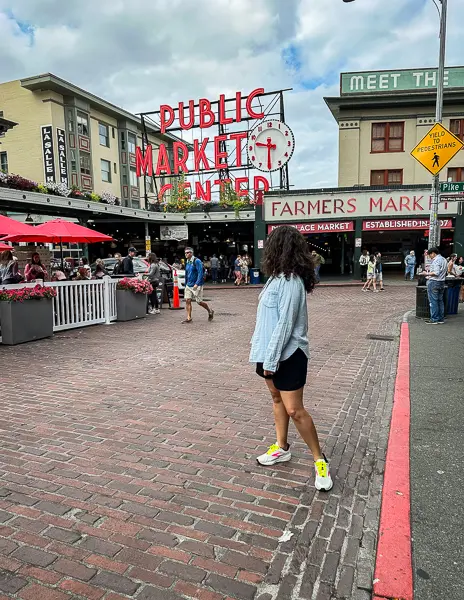 woman standing outside of pike place market sign